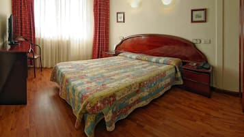 A bedroom with a wooden bed, a desk, and a chair. There are curtains on the window, and a framed picture on the wall.