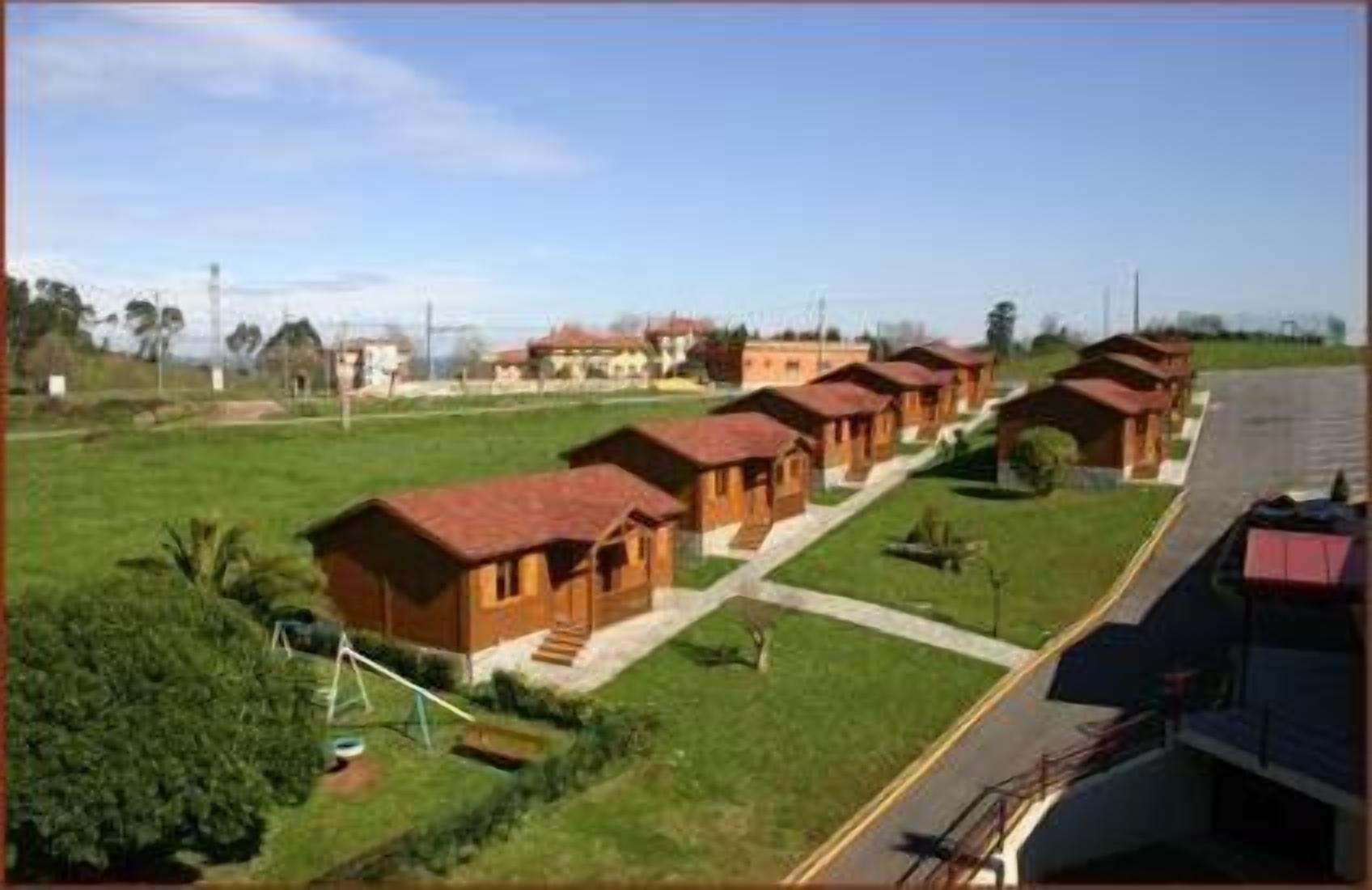 Une rangée de cabanes en bois aux toits rouges, disposées en ligne le long d’une route.