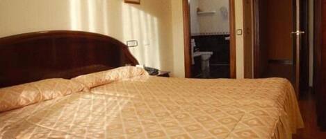A neatly made bed with a patterned bedspread, a wooden headboard, and a small bedside table.