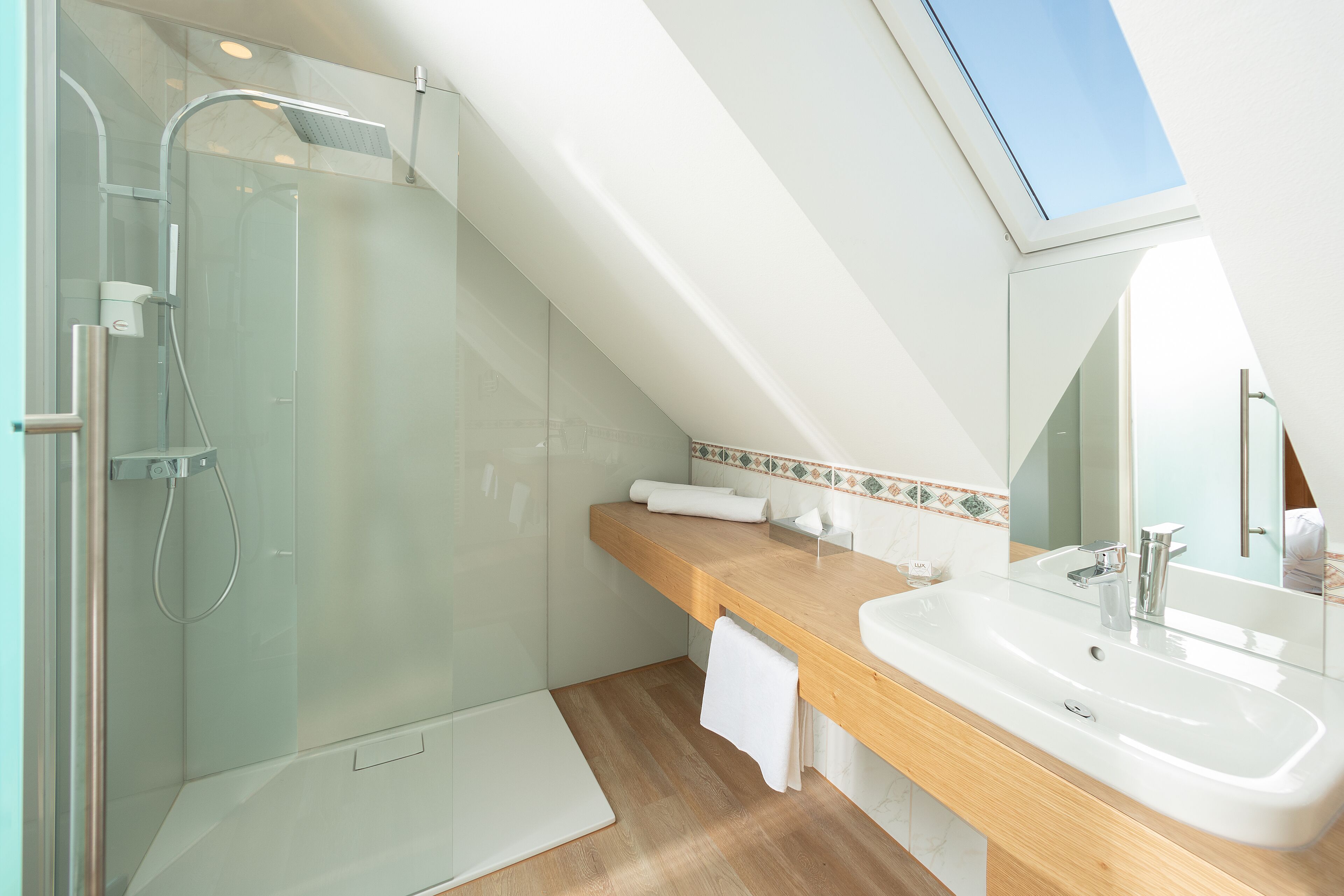 Un baño moderno con ducha envuelta en vidrio, tocador de madera, espejo grande y tragaluz.