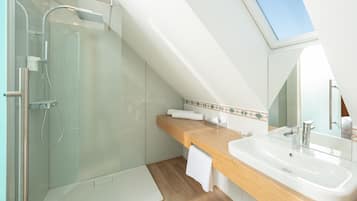 Un baño moderno con ducha envuelta en vidrio, tocador de madera, espejo grande y tragaluz.