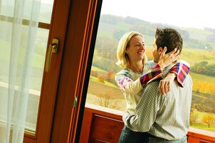 Una pareja abrazándose frente a una ventana con vistas a un paisaje pintoresco.