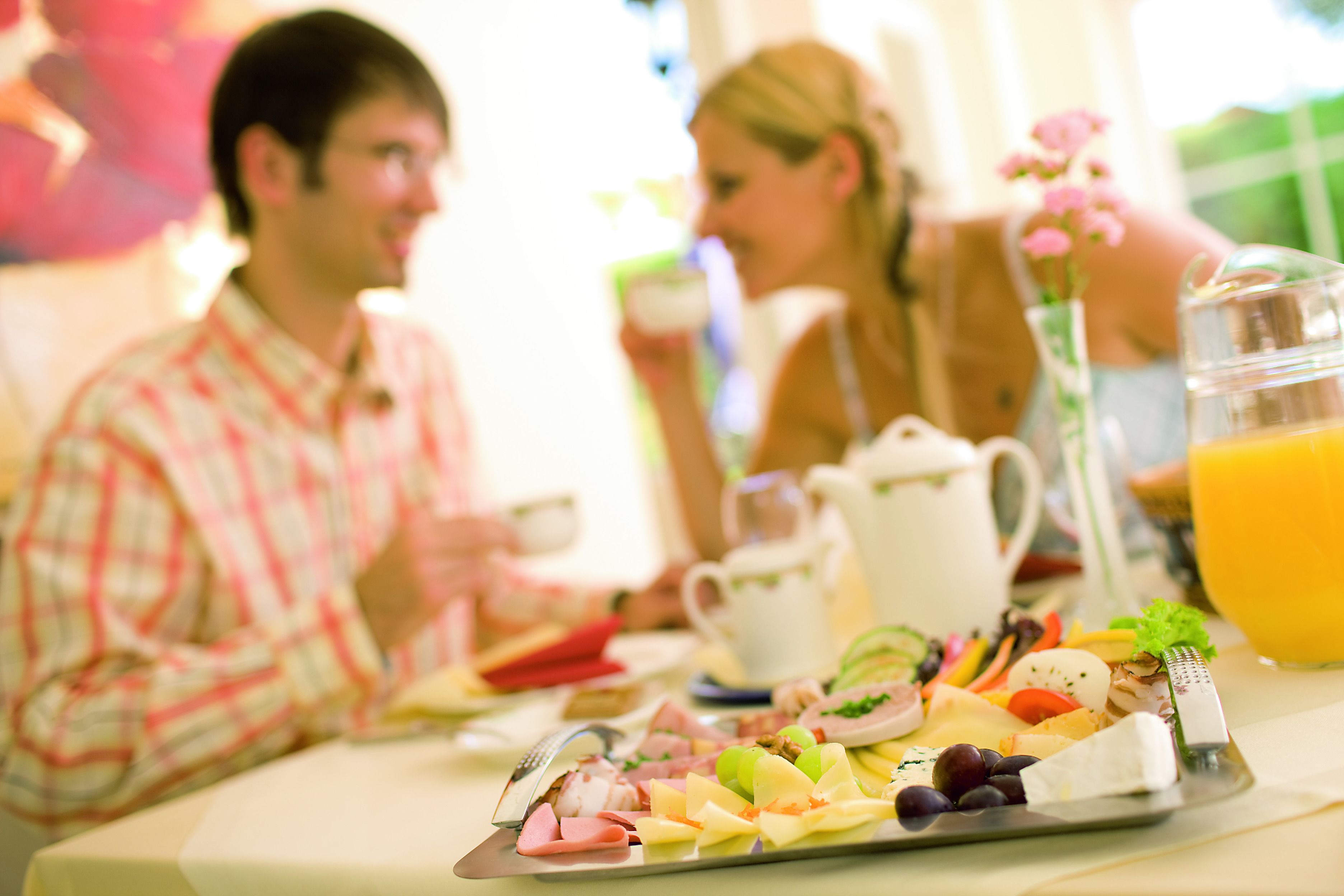 A breakfast setting with a variety of foods on a tray, including fruits, cheeses, and meats.
