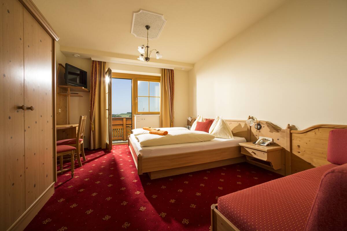 Une chambre d’hôtel avec un lit, un bureau, une chaise, une télévision et une fenêtre avec des rideaux.