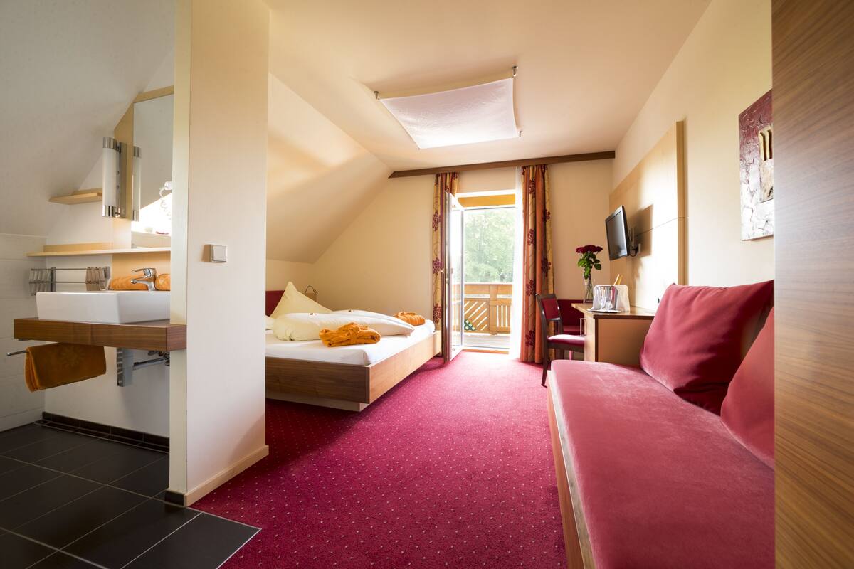 Une chambre d’hôtel comprenant un lit, un canapé, une télévision, une salle de bain avec un lavabo et une fenêtre avec des rideaux.