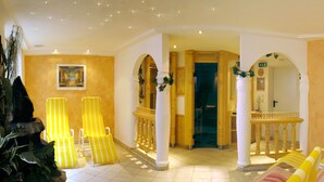 A hotel lobby with yellow-striped chairs, a fountain, and a staircase with white columns. - Hotel Alpenherz (Gerlos)