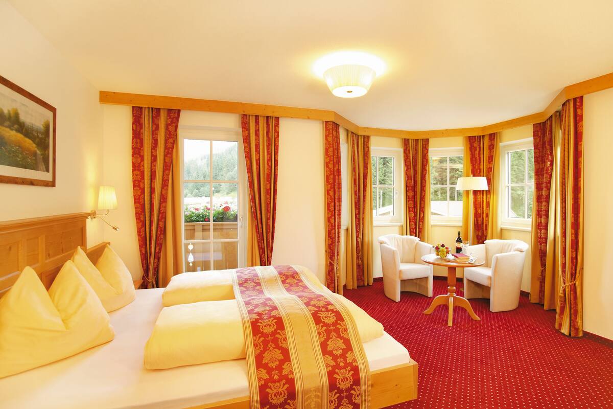 A hotel room with a bed, two chairs, a small table, and a window with curtains.