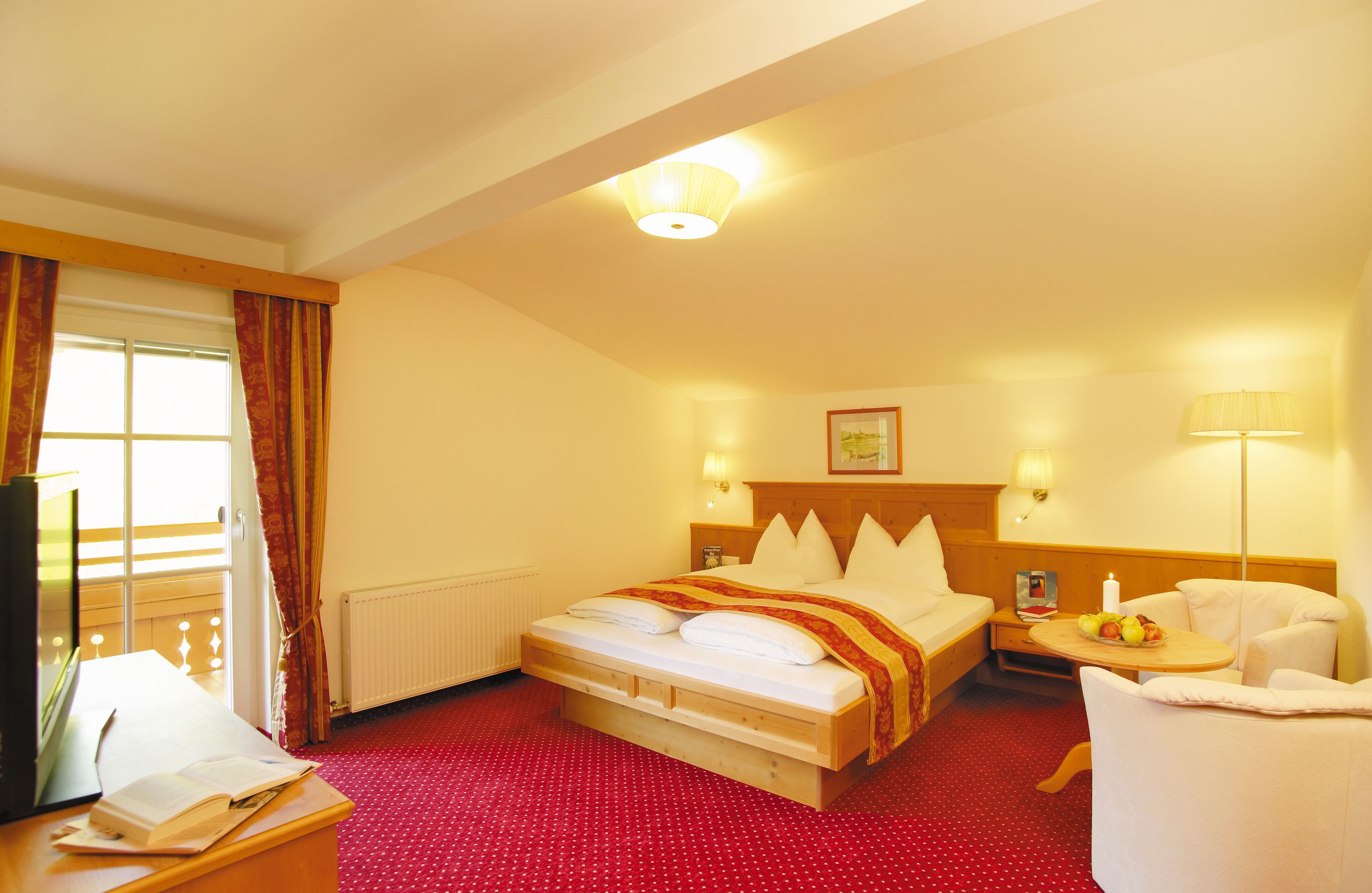 Ein Hotelzimmer mit einem Bett, einem Schreibtisch mit Lampe, einem Sessel und einem kleinen Tisch mit Obst.
