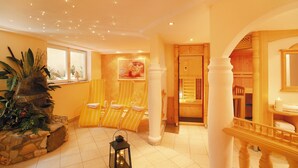 A spa area with a stone fountain, yellow-striped lounge chairs, and a wooden reception desk. - Hotel Alpenherz (Gerlos)