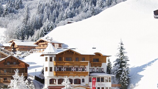 A snow-covered mountain landscape with a wooden chalet-style building featuring balconies and a red flag. - Hotel Alpenherz (Gerlos)