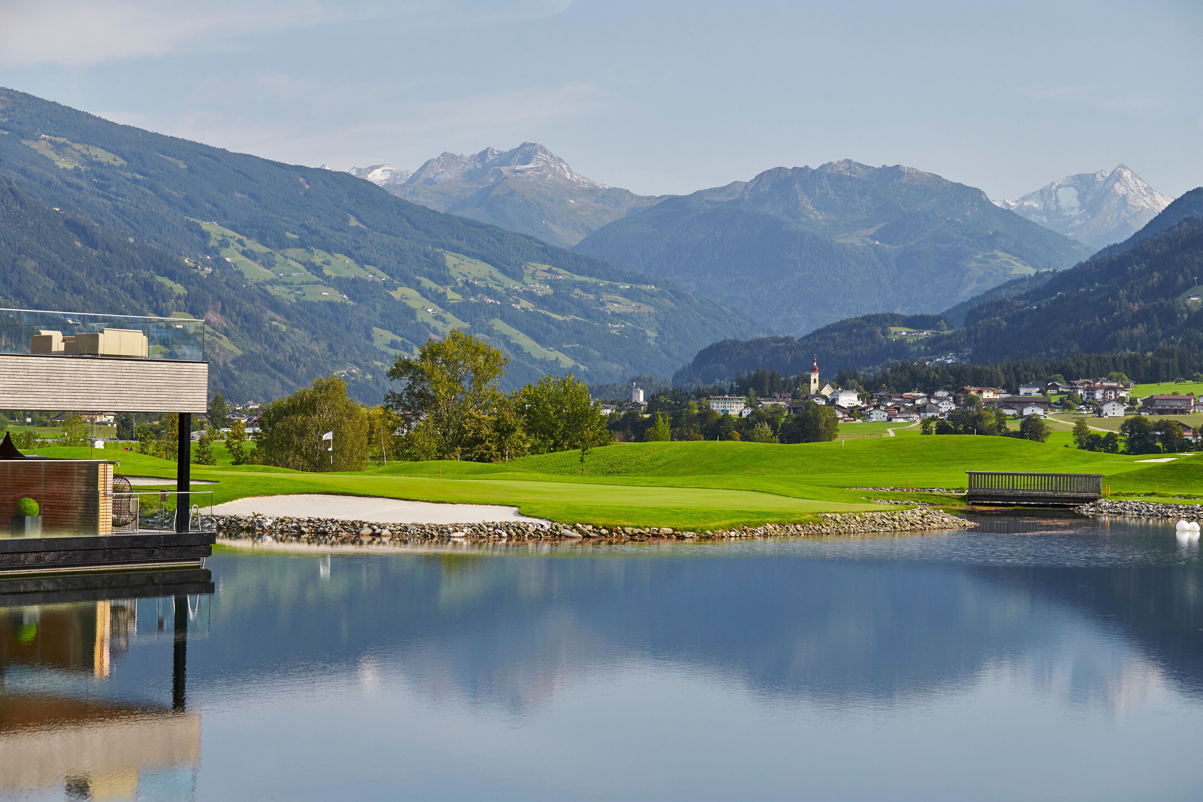 Uitzicht op een meer, met een golfbaan, bergen en een klein stadje op de achtergrond.