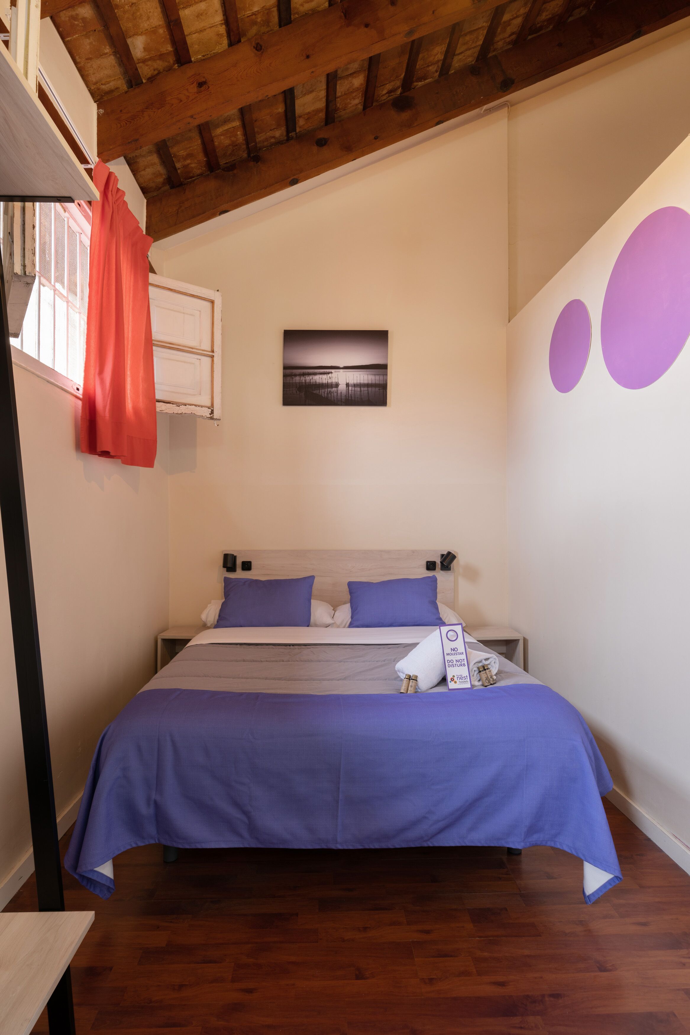 A bedroom with a bed, wooden floor, and a ceiling with exposed beams.