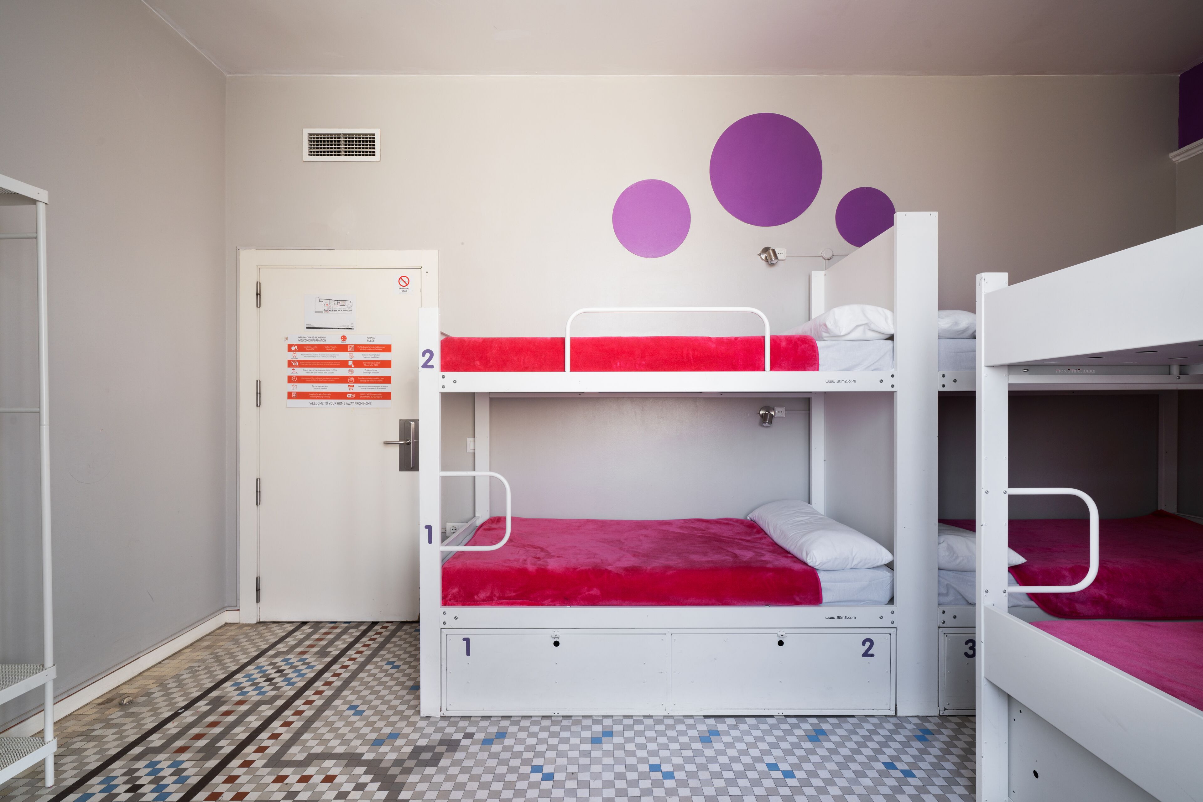 A dormitory room with bunk beds, a door with a notice, and a patterned floor.