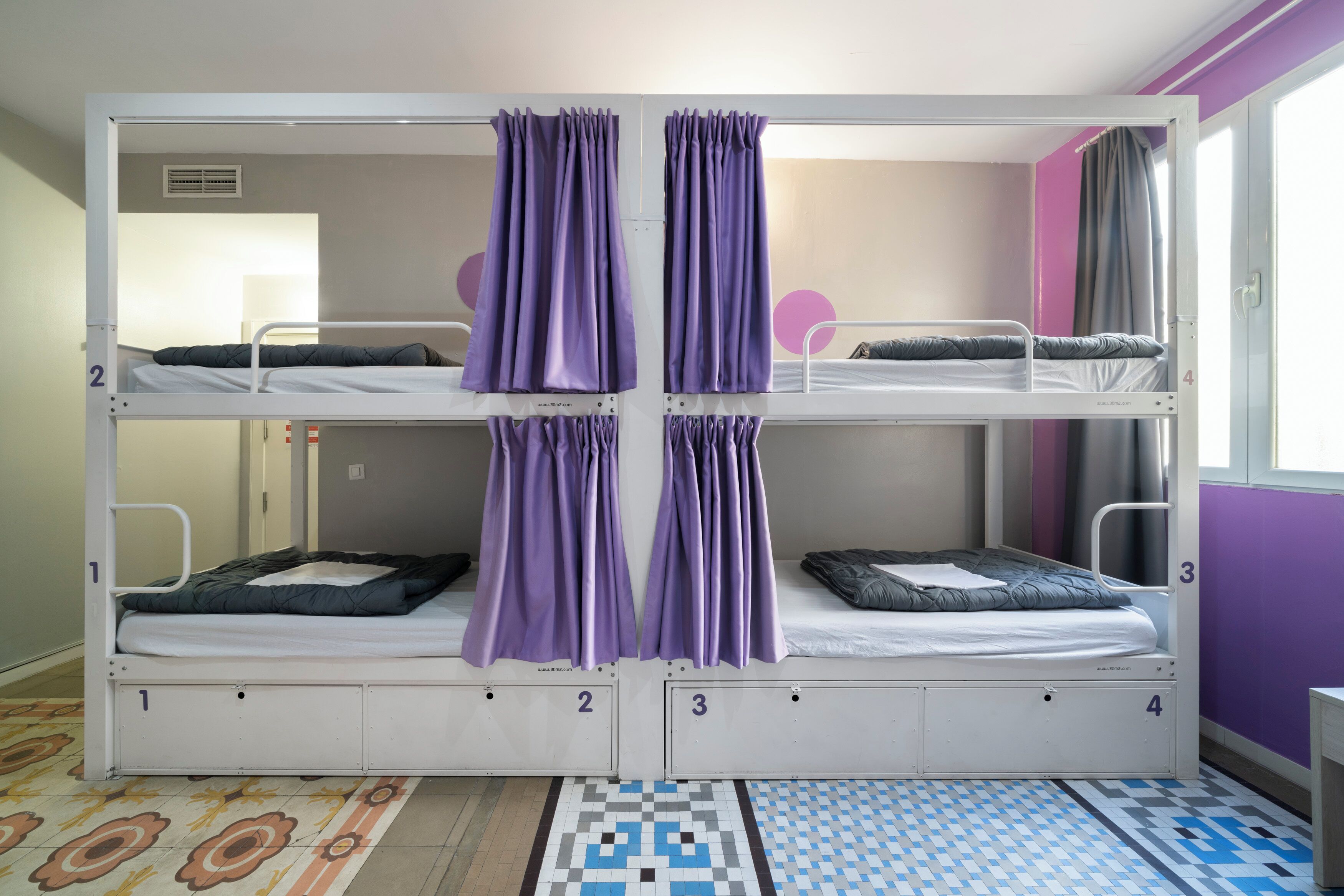 Dormitorio con literas, cuatro camas numeradas del 1 al 4 y cortinas moradas.