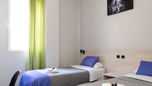 A hotel room with two beds, a window with green curtains, a checkered floor, and a painting on the wall.