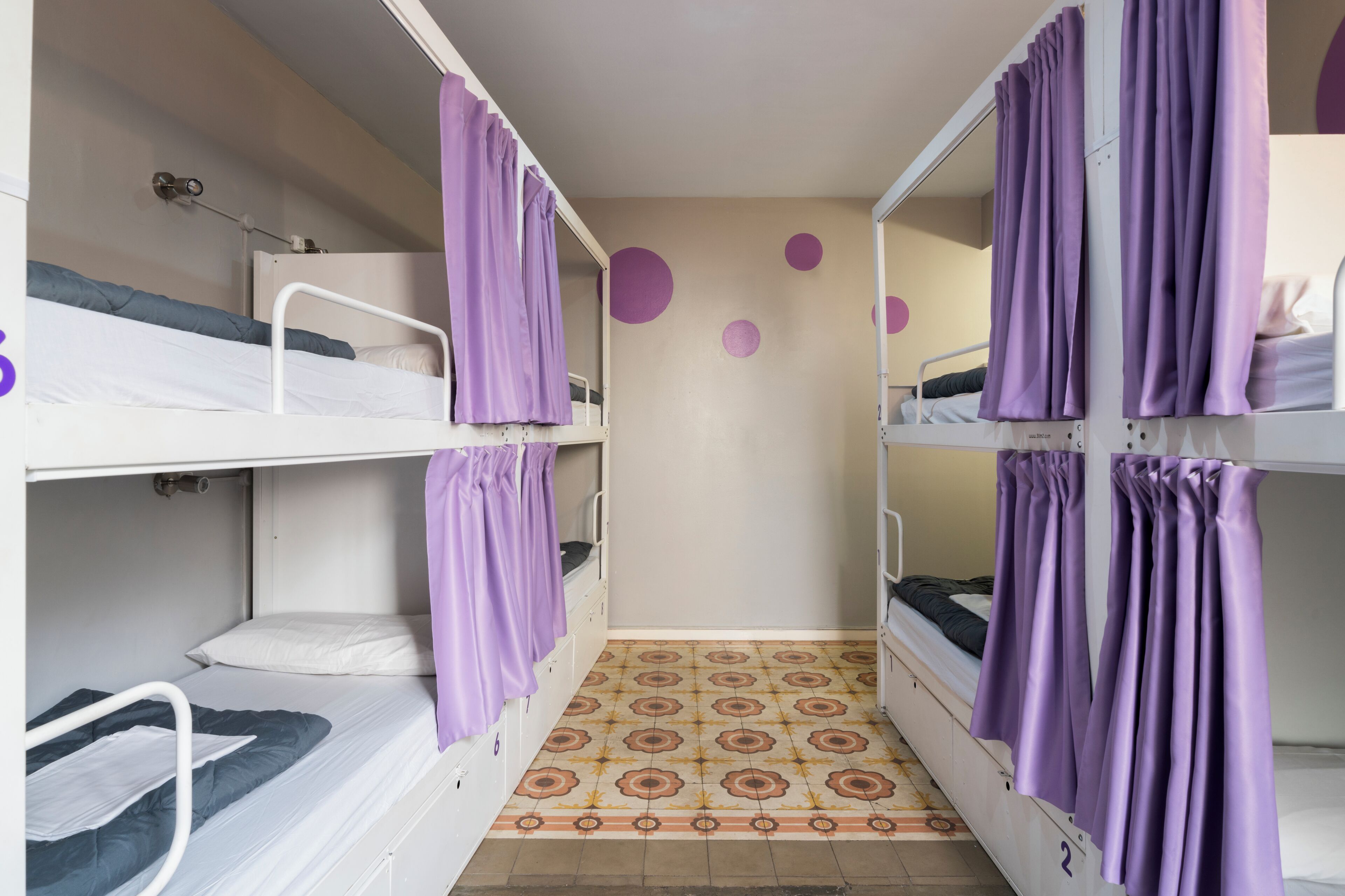 Un dormitorio con literas, cortinas moradas y un suelo estampado.
