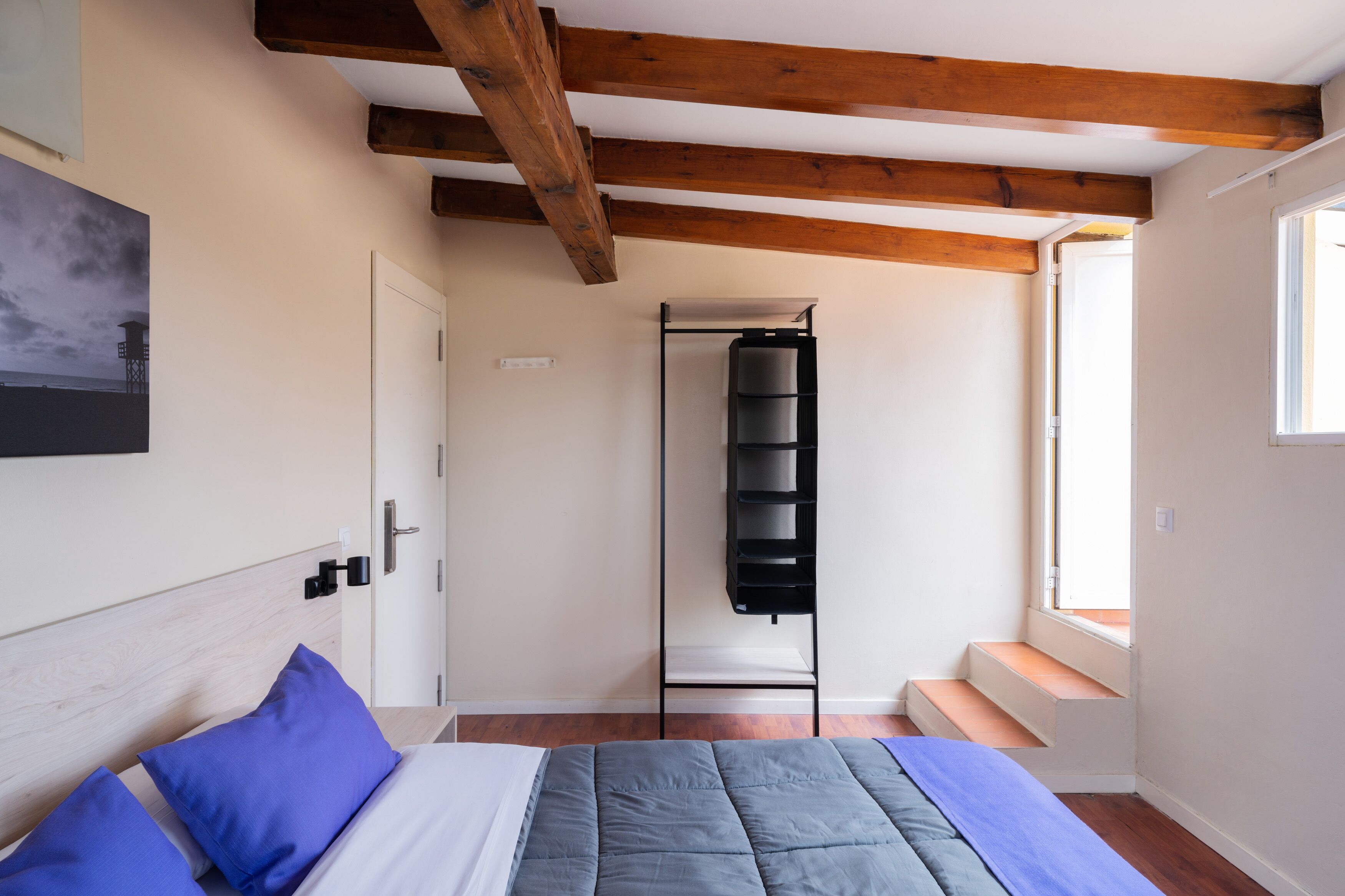 Une chambre à coucher avec un lit, un plafond en bois, une fenêtre et une étagère fixée au mur.