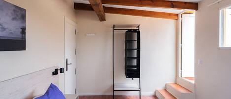 Ein Schlafzimmer mit einem Bett, einer Holzbalkendecke, einem Fenster und einem Wandregal.