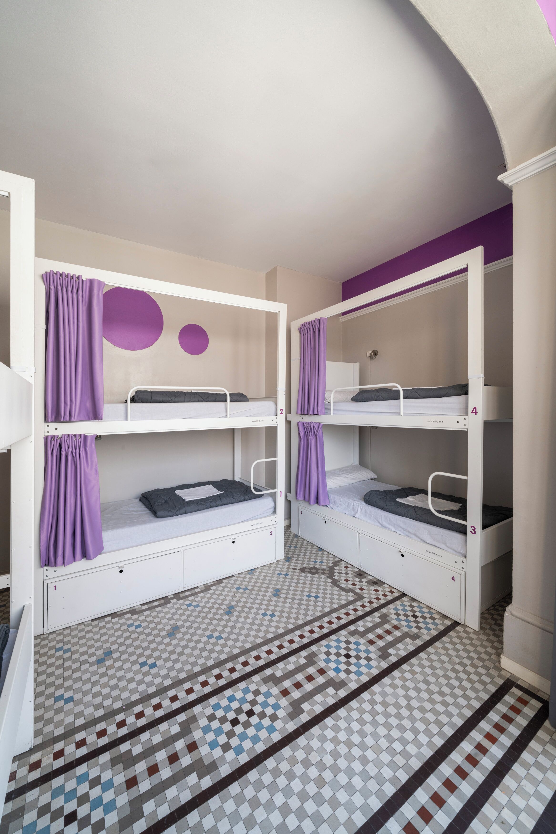 Ein Zimmer mit Etagenbetten, einem gemusterten Boden und einer violetten Wand.