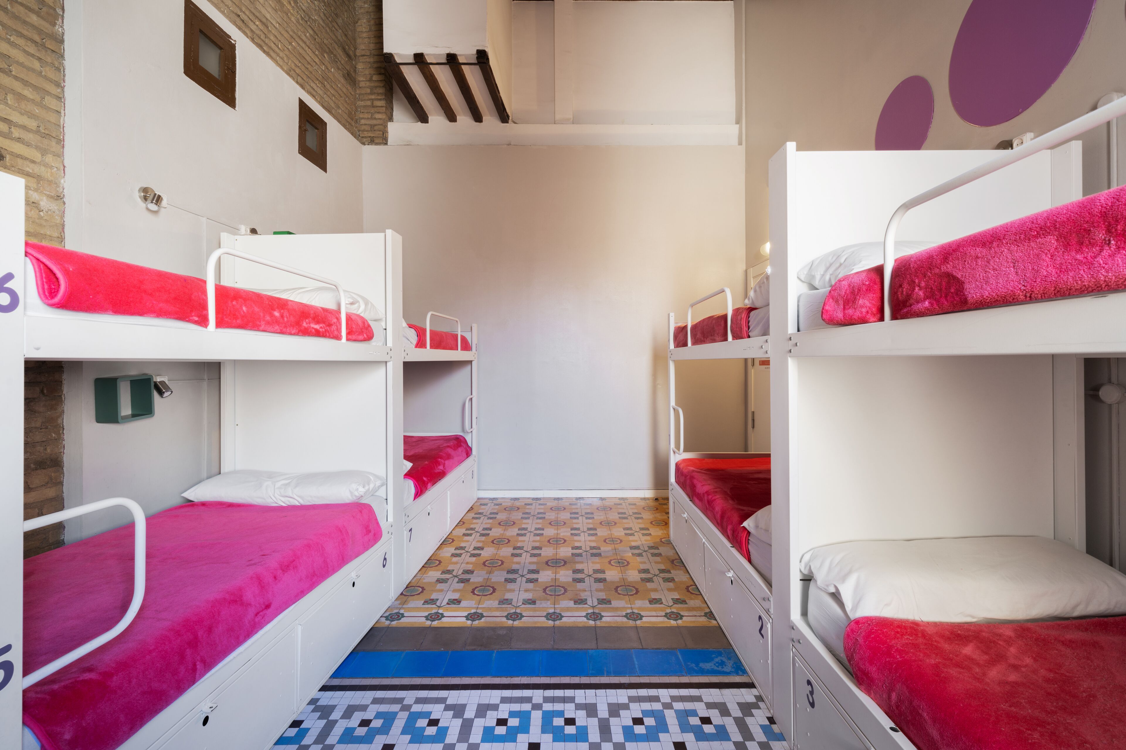 A dormitory room with bunk beds, a patterned floor, and a small window.