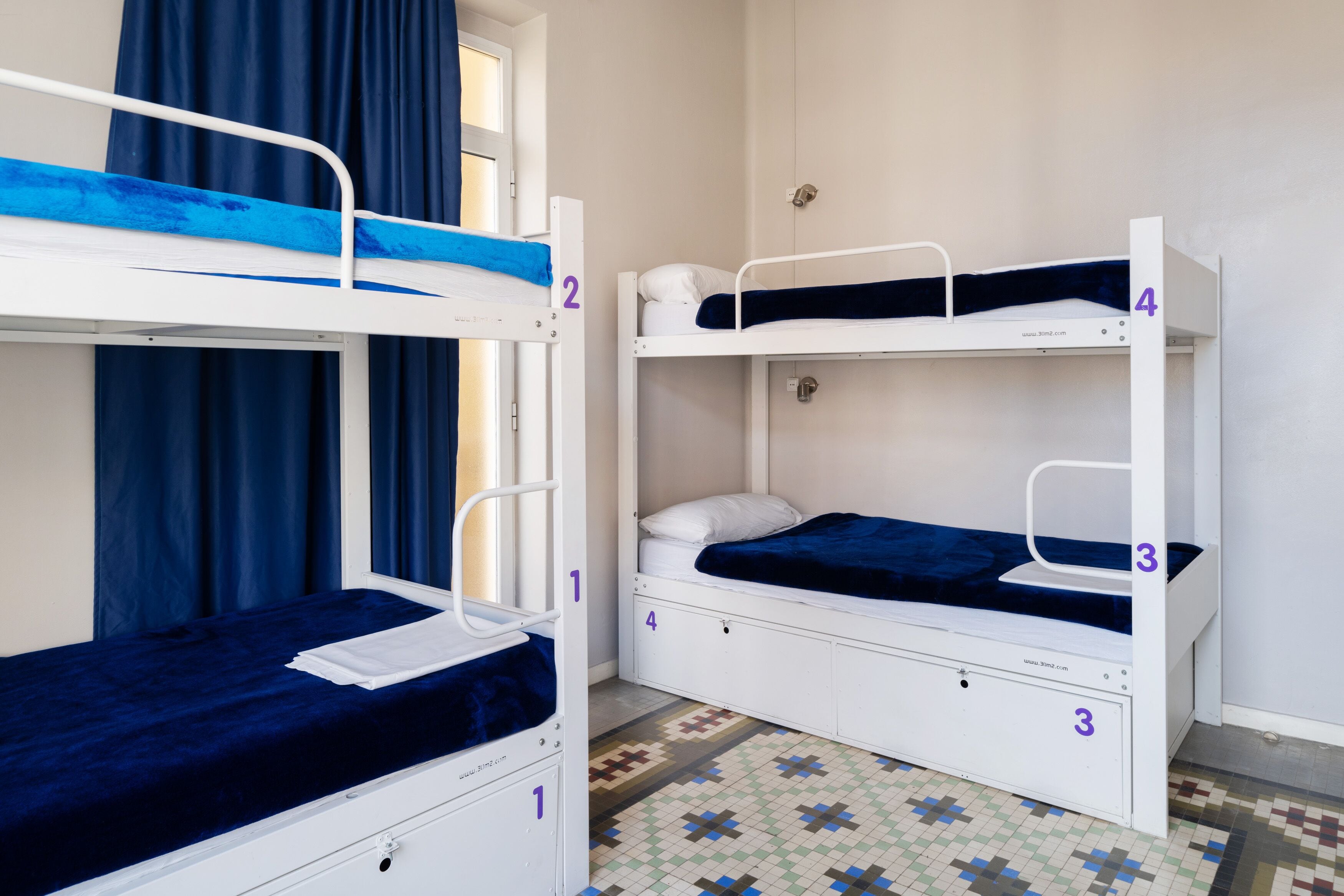 A room with bunk beds labeled 1 to 4, a patterned floor, and a window with blue curtains.