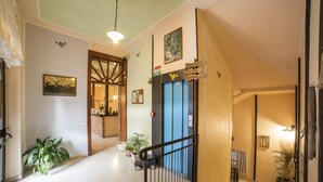 Un couloir d’hôtel avec une porte en bois, un ascenseur bleu et une plante en pot.