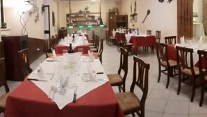 Un restaurant avec de nombreuses tables dressées pour le service, des chaises en bois et un mur de pierre en arrière-plan.