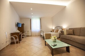 A hotel room with a bed, a sofa, a coffee table, a TV, and a desk with chairs.