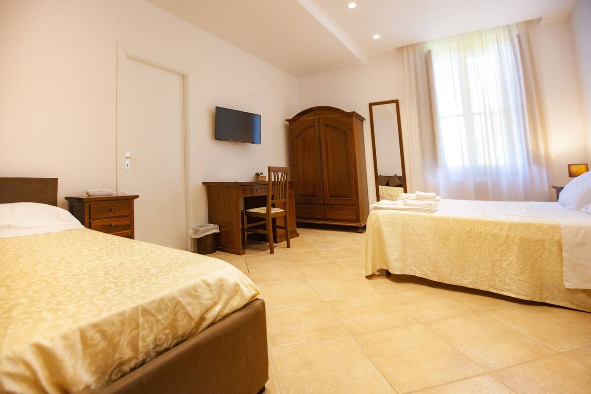 A hotel room with two beds, a desk, a chair, a wardrobe, a television, and a window with curtains.