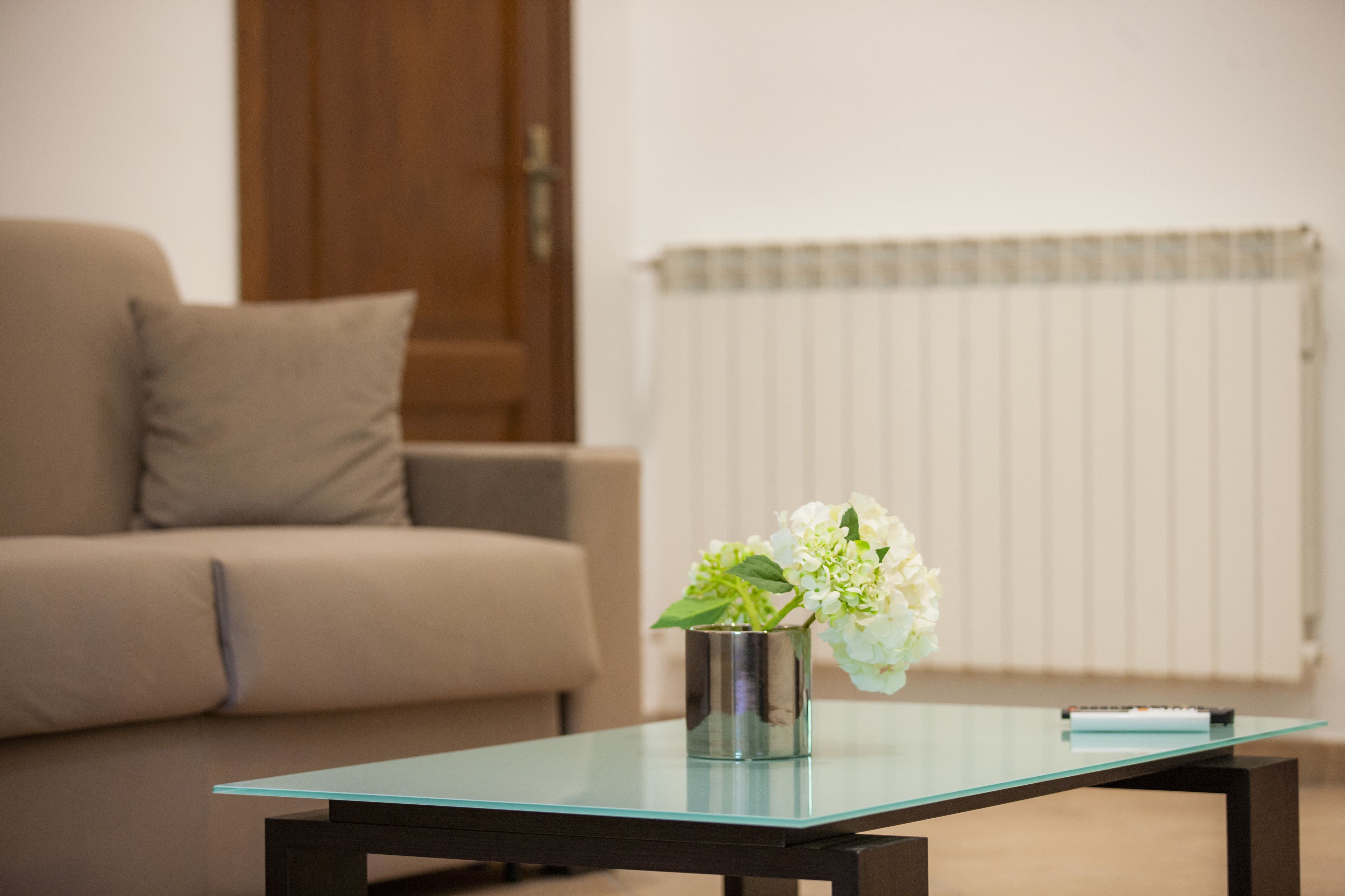 A modern living room with a glass-top coffee table, a beige sofa, and a radiator in the background.