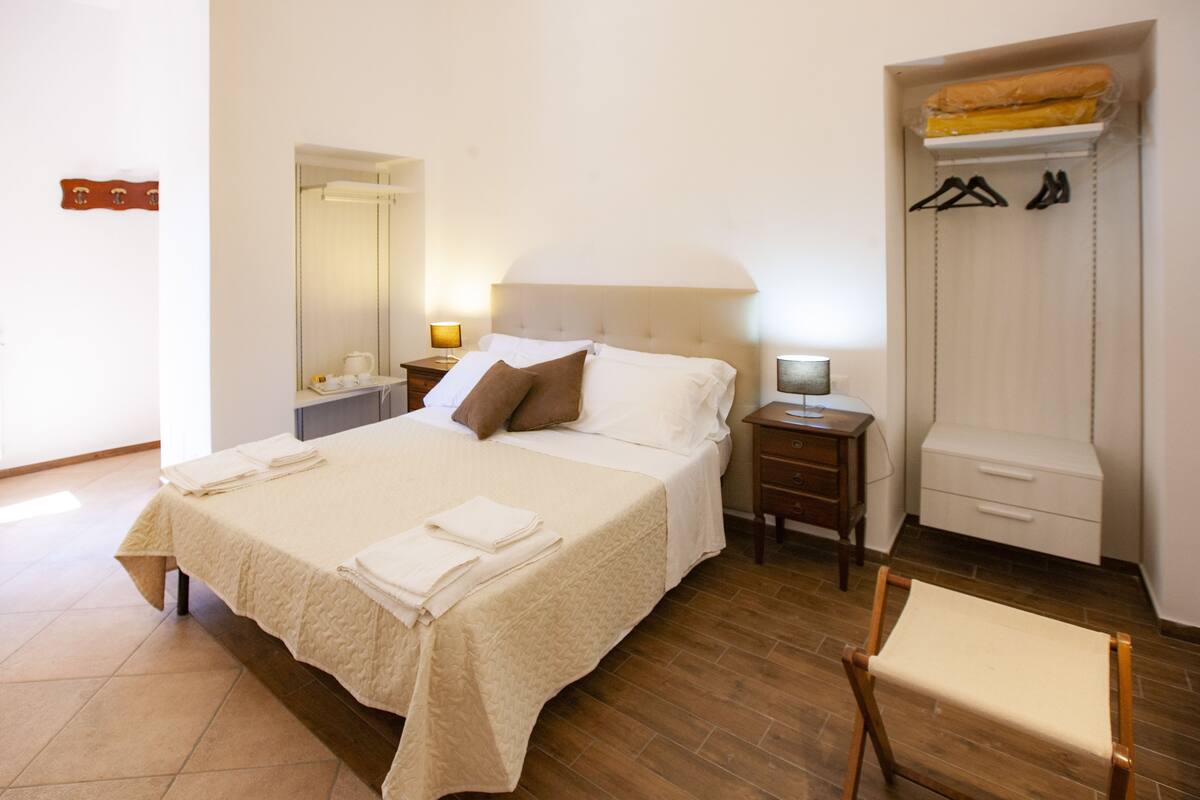 A neatly arranged hotel room with a large bed, a bedside table, a chair, a wardrobe, and a mirror.