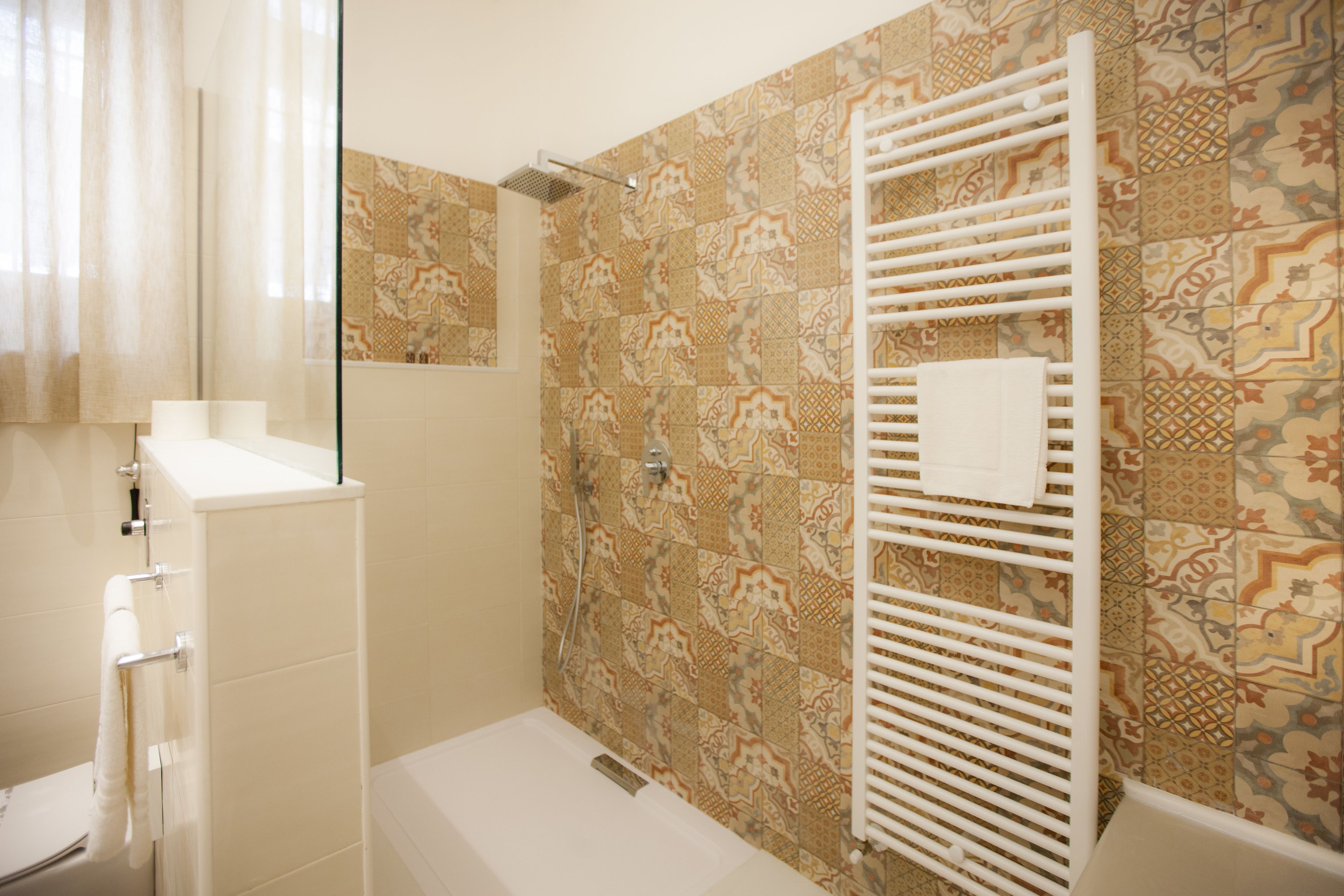 A bathroom with patterned tiles, a white bathtub, a glass shower enclosure, and a towel rack.