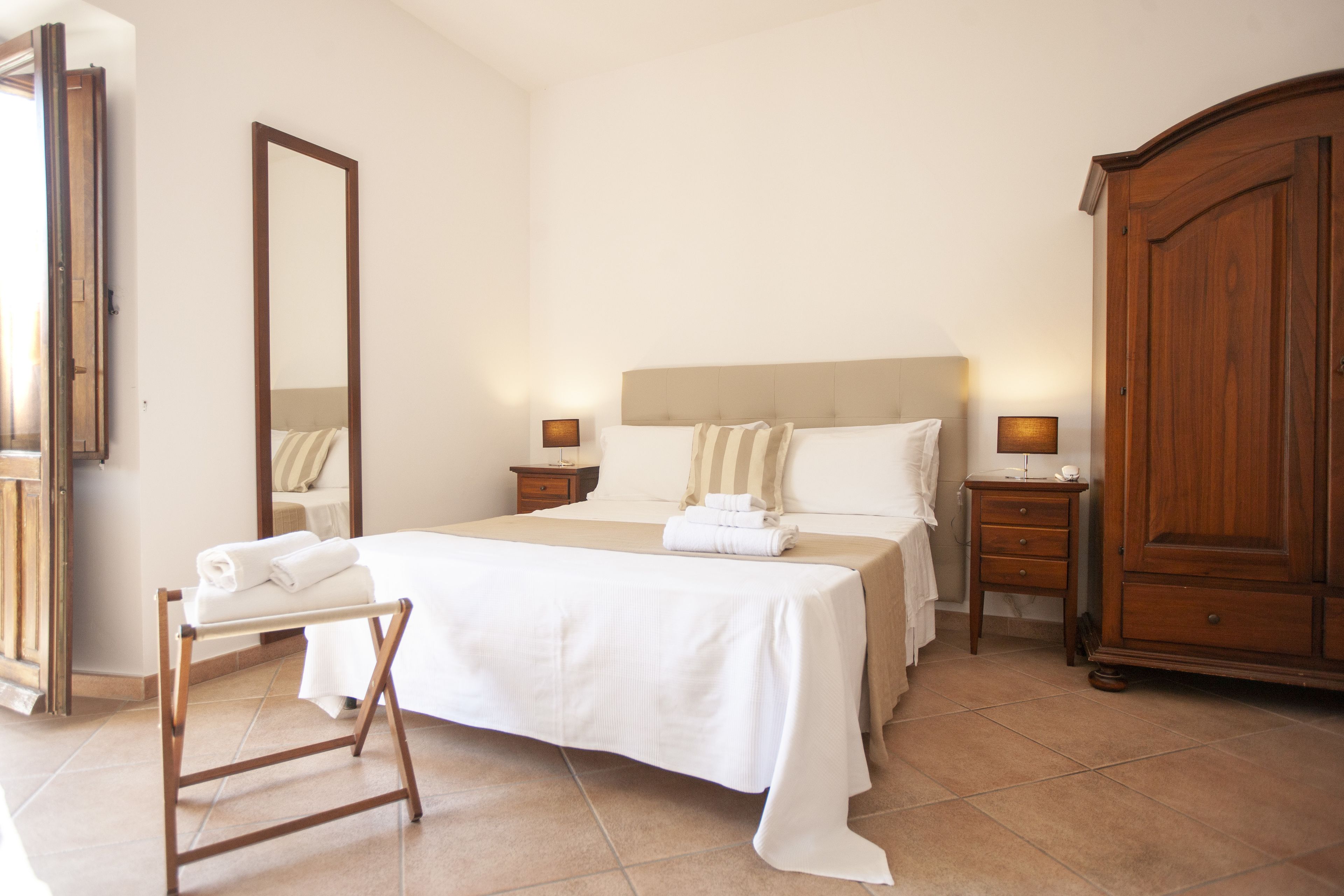 Une chambre d’hôtel avec un grand lit, une armoire en bois, une table de chevet et un miroir.