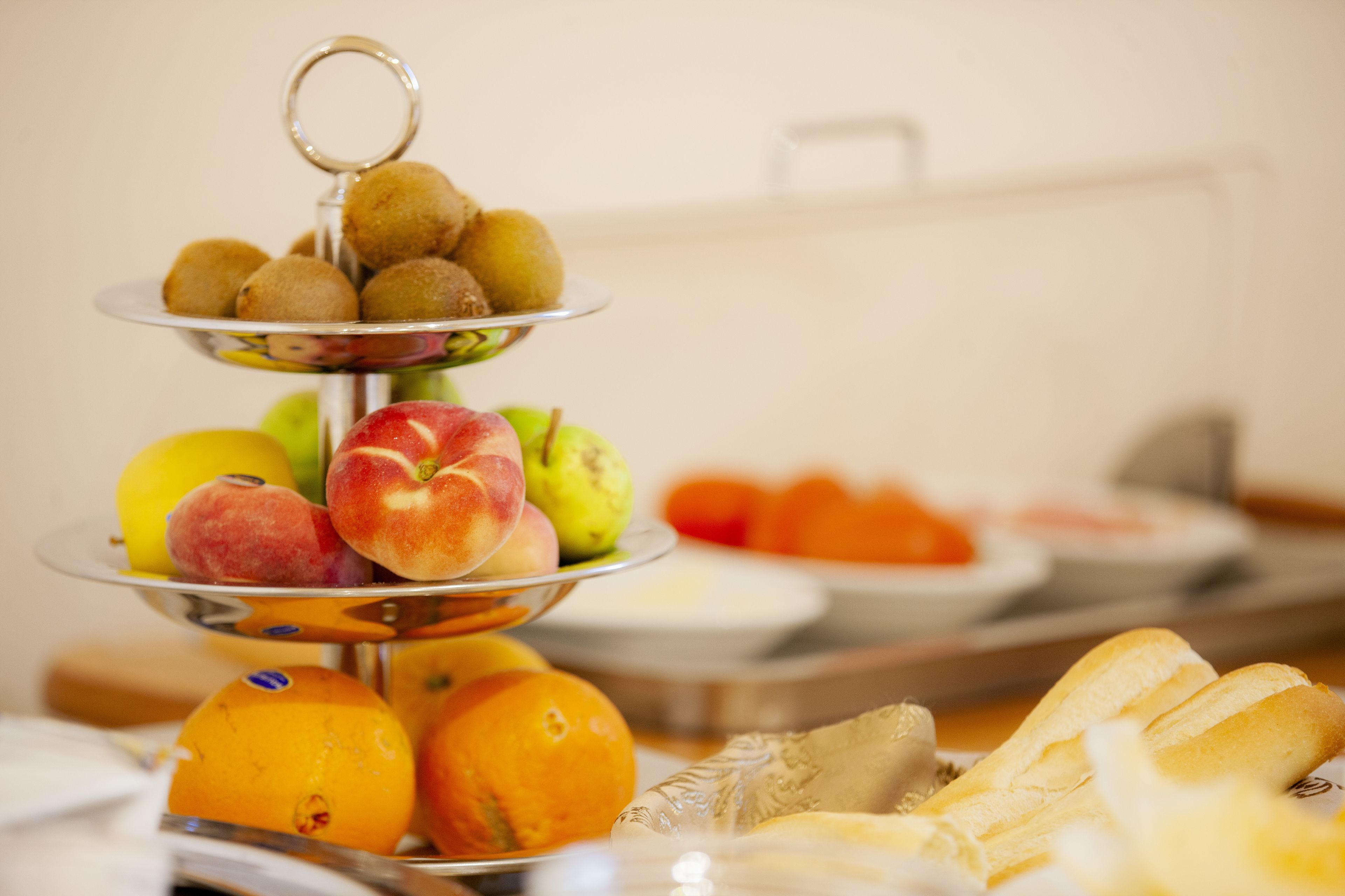 A multi-tiered fruit stand with various fruits and a plate of pastries.