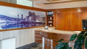 Een moderne hotel lobby met een gebogen receptiebalie, een groot stadsgezicht muurschildering, houten lambrisering en een plank met ringmappen en bekers.