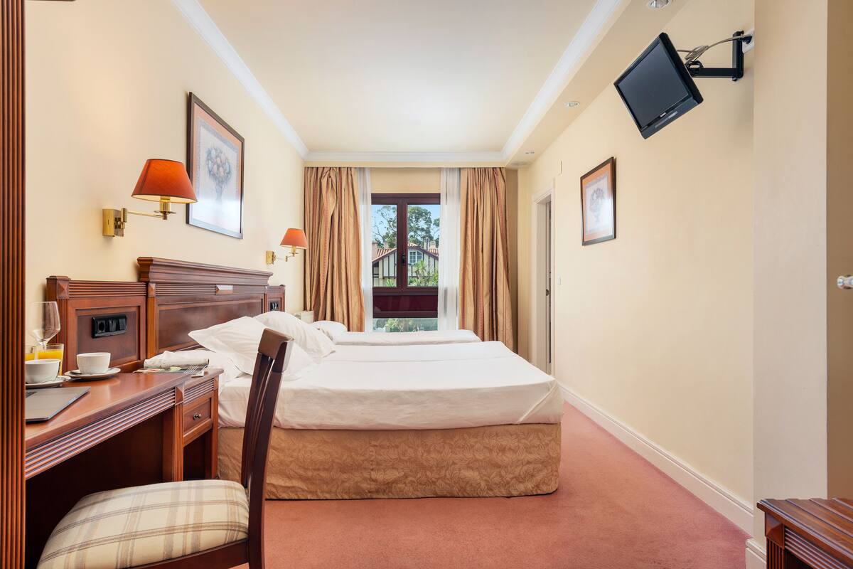 Ein Hotelzimmer mit Bett, Schreibtisch mit Stuhl, Wandfernseher und einem Fenster mit Vorhängen.