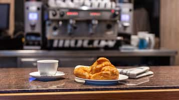 Een croissant op een bord met een kopje op een schotel, en een koffieapparaat op de achtergrond.