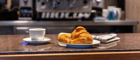 A croissant on a plate with a cup on a saucer, and a coffee machine in the background.