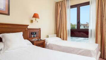 Habitación de hotel con dos camas, una mesita de noche con lámpara, una ventana con cortinas y vistas al exterior.