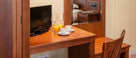 A wooden desk with a television, two wine glasses, a cup, and a saucer.