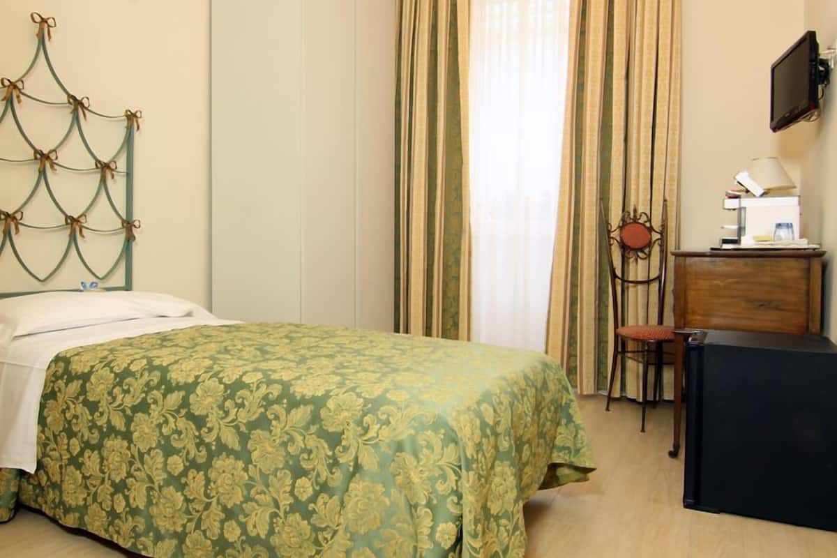 A hotel room with a bed, a desk, a chair, a television, and a window with curtains.
