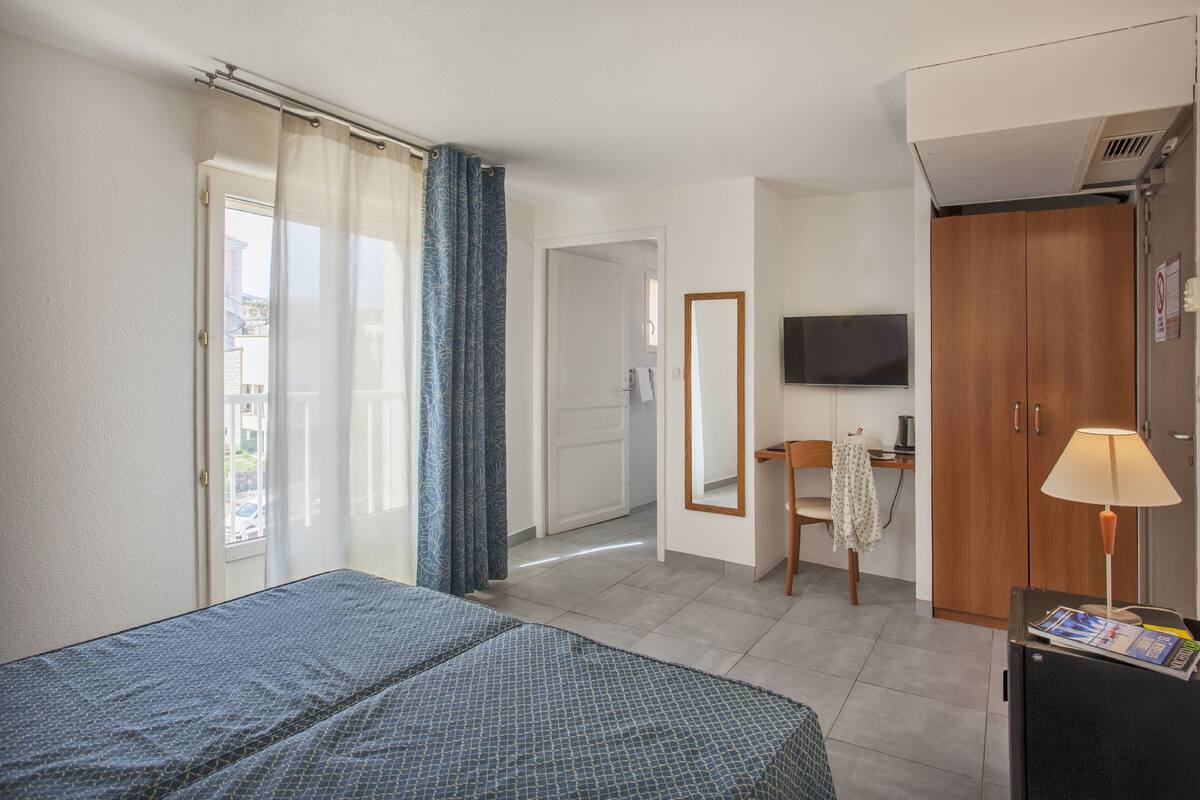 A hotel room with a bed, a desk, a chair, a TV, and a wardrobe.