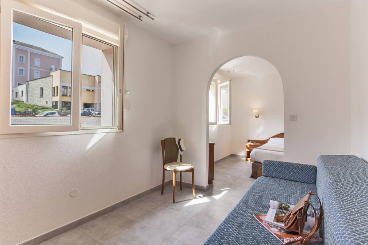 A modern hotel room with a large window, a sofa, a chair, and a bed.