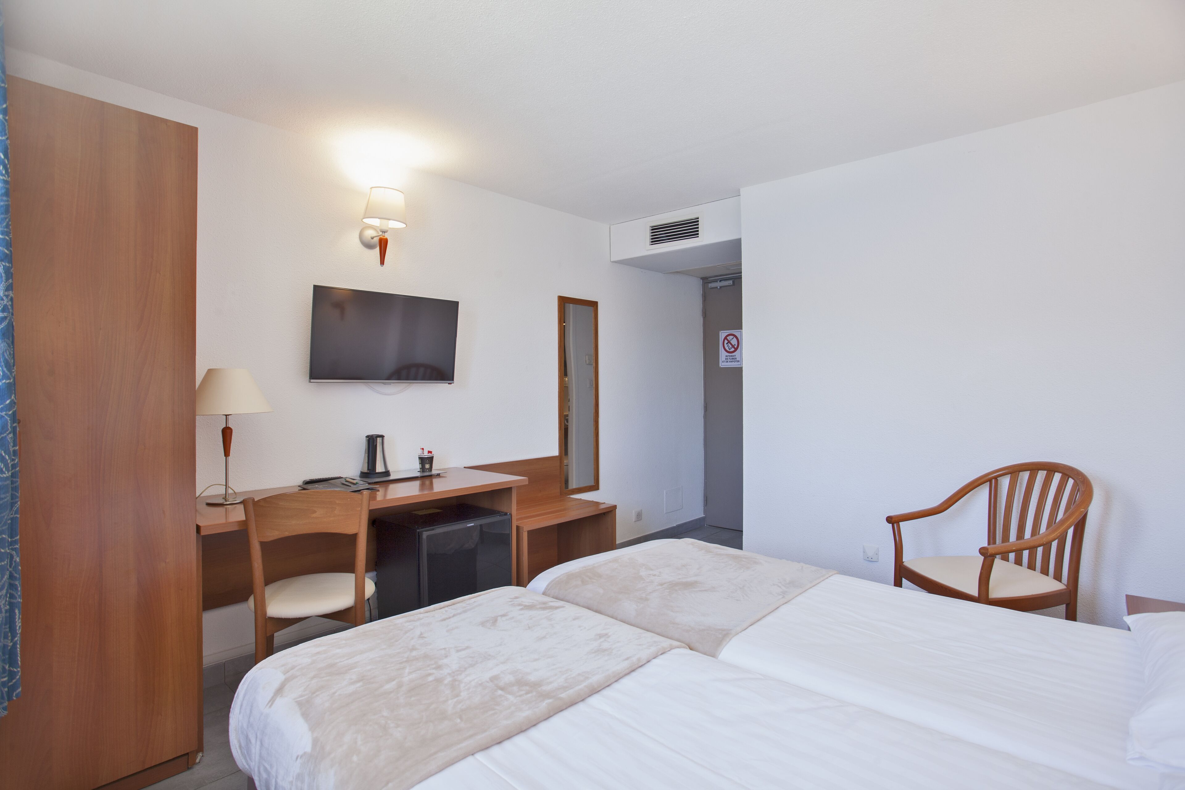 Une chambre d’hôtel comprenant un lit, un bureau avec une chaise, une télévision et un miroir.