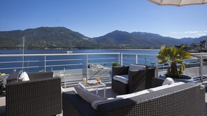 A terrace with wicker furniture, a table with drinks, and a view of a lake and mountains. - Hôtel Le Neptune (Propriano)