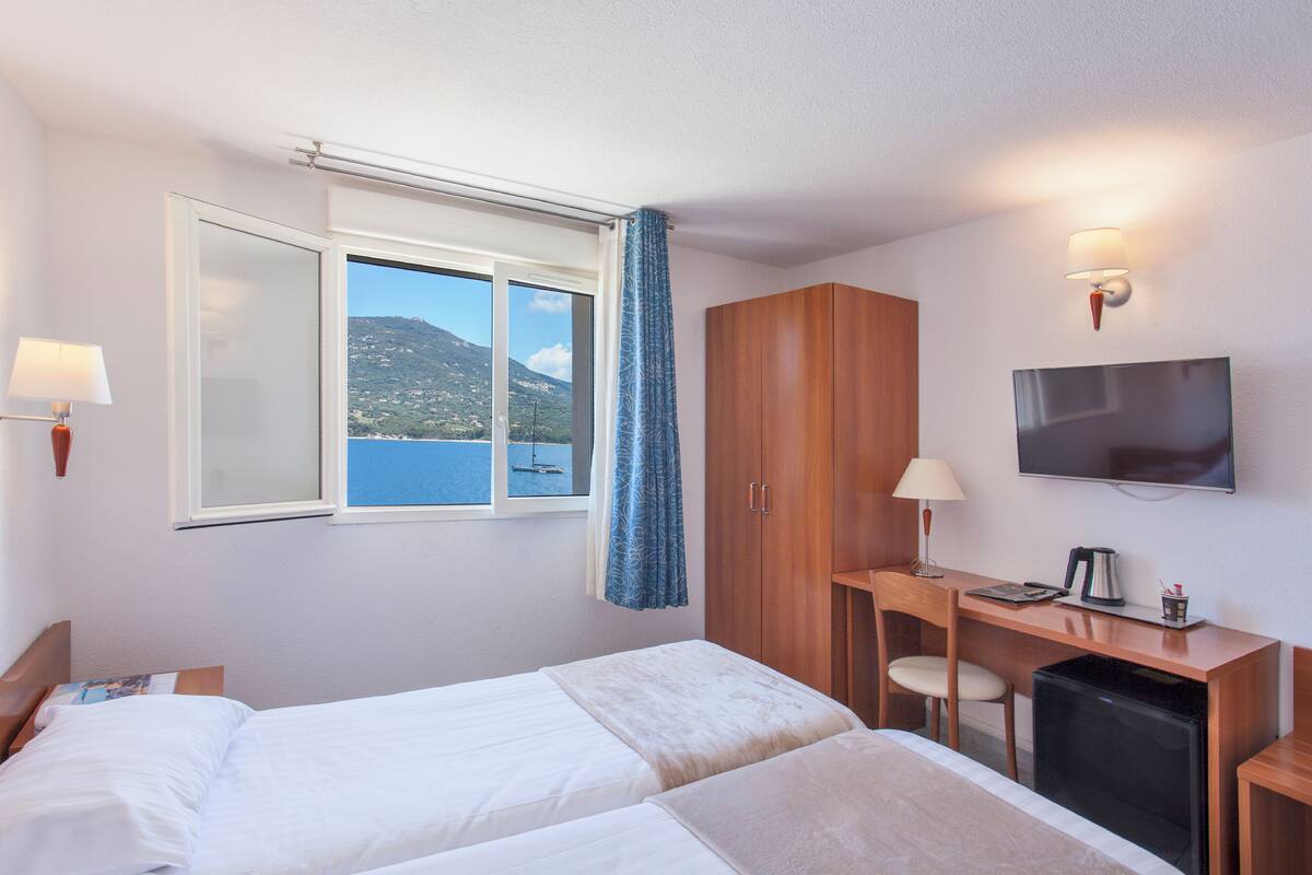 A hotel room with two beds, a desk, a TV, and a view of a mountainous landscape.