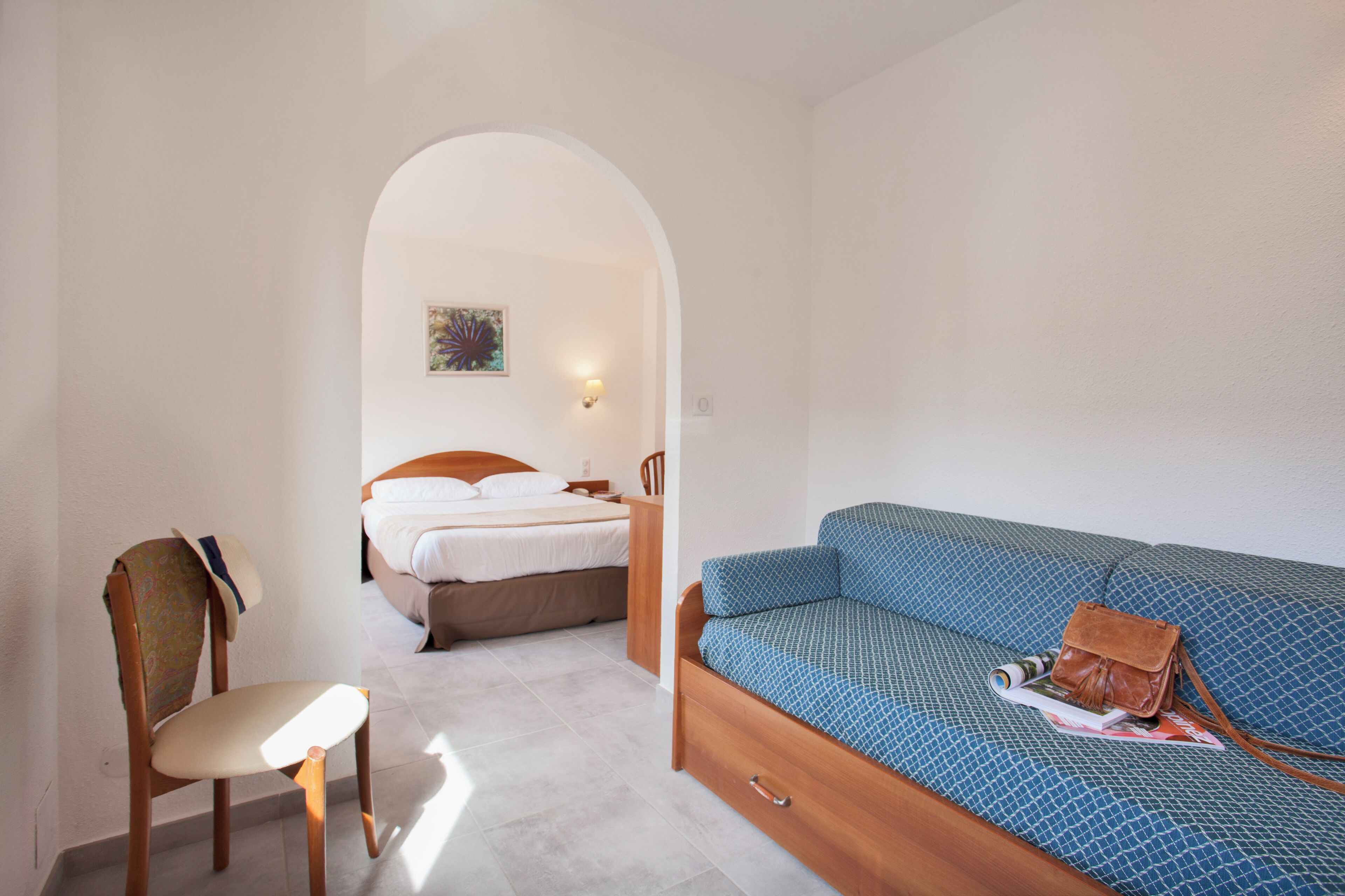 A bedroom with a bed, a wooden chair, a sofa, and a small table.