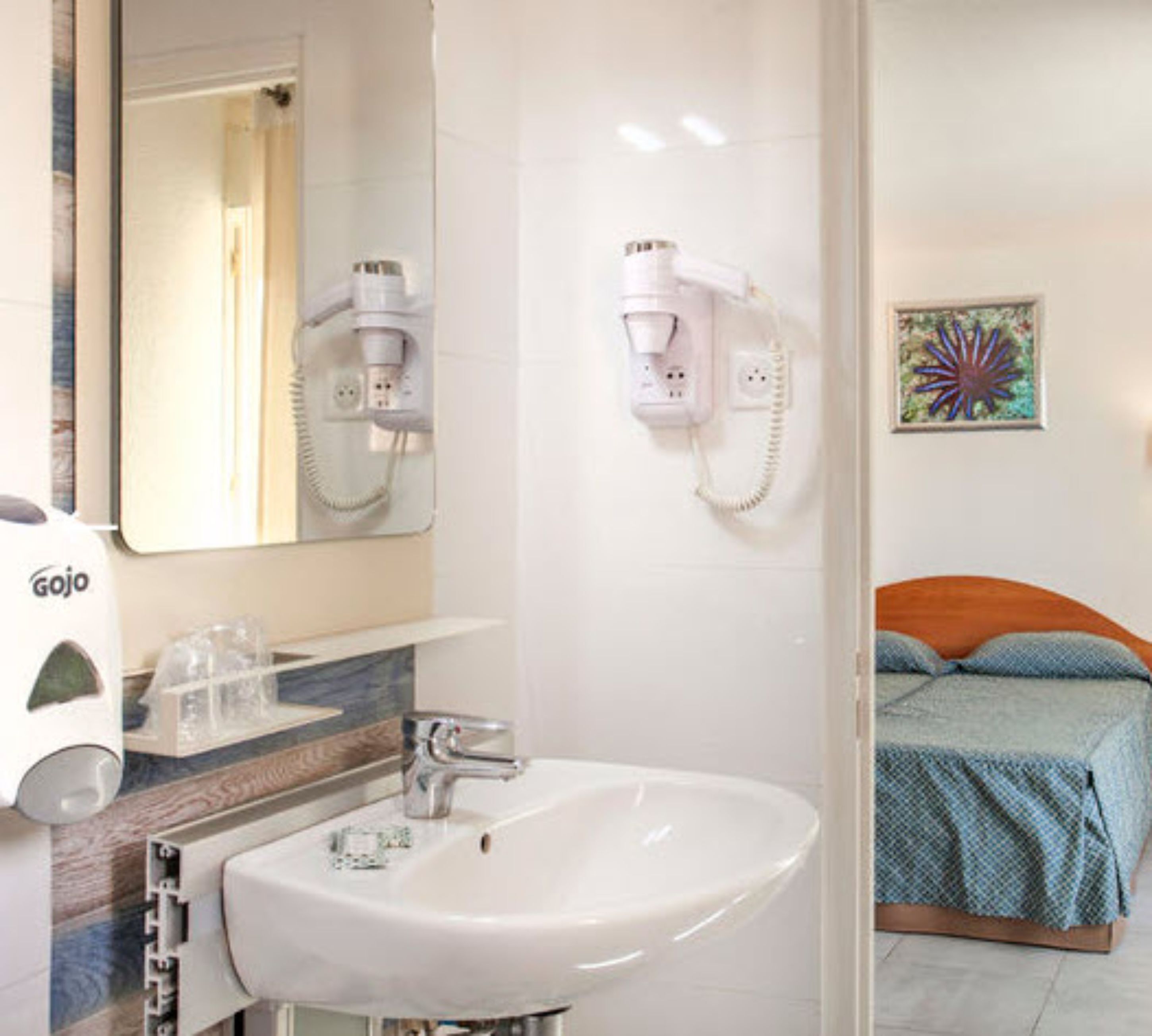Un baño con lavamanos, espejo, secador de pelo y un cuadro en la pared.