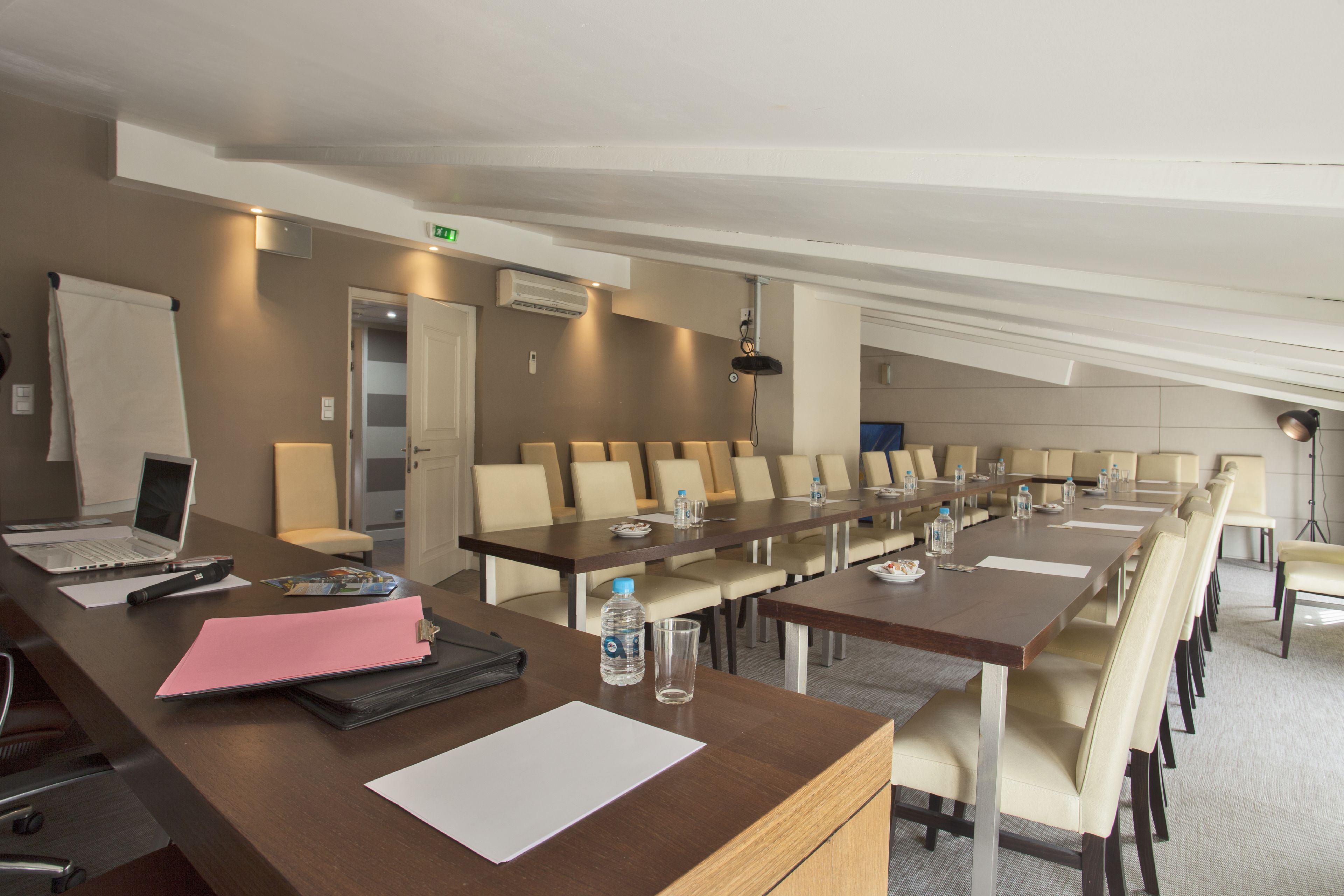 A conference room with long tables, chairs, a laptop, a water bottle, and a whiteboard.