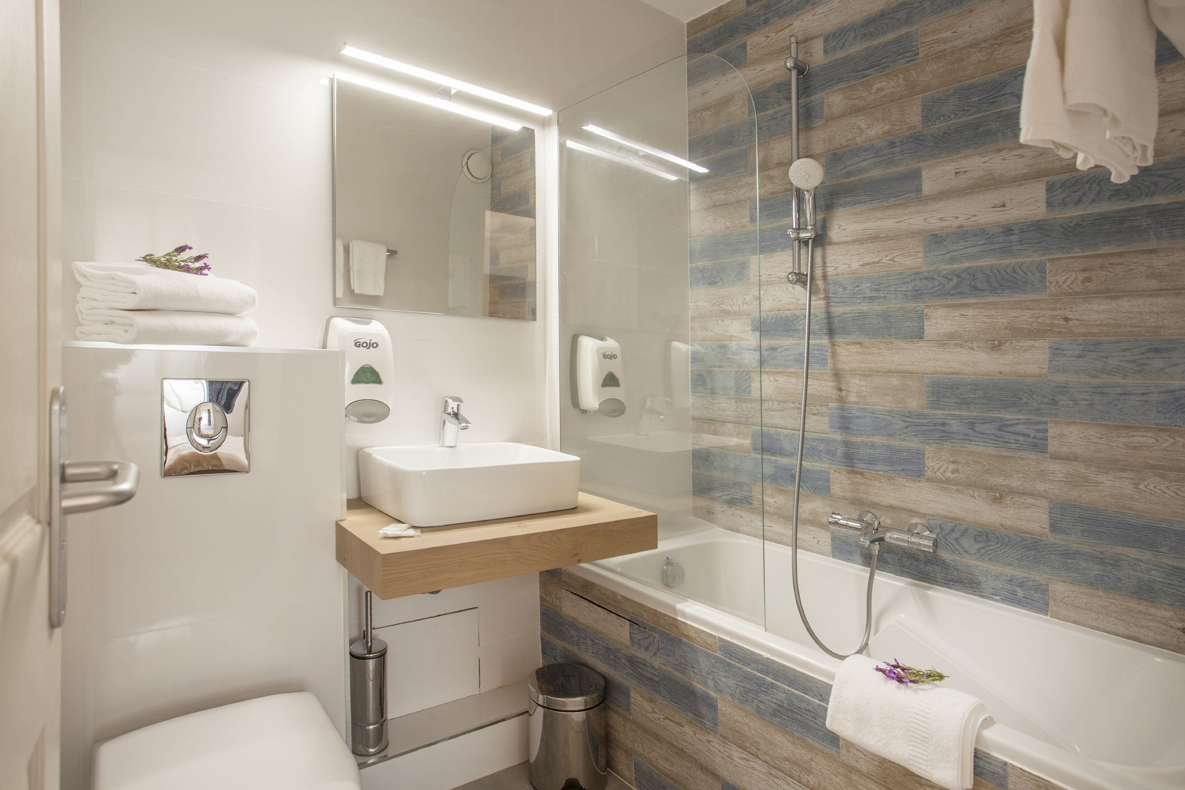 Un baño moderno con ducha envuelta en vidrio, lavamanos blanco y tocador de madera.